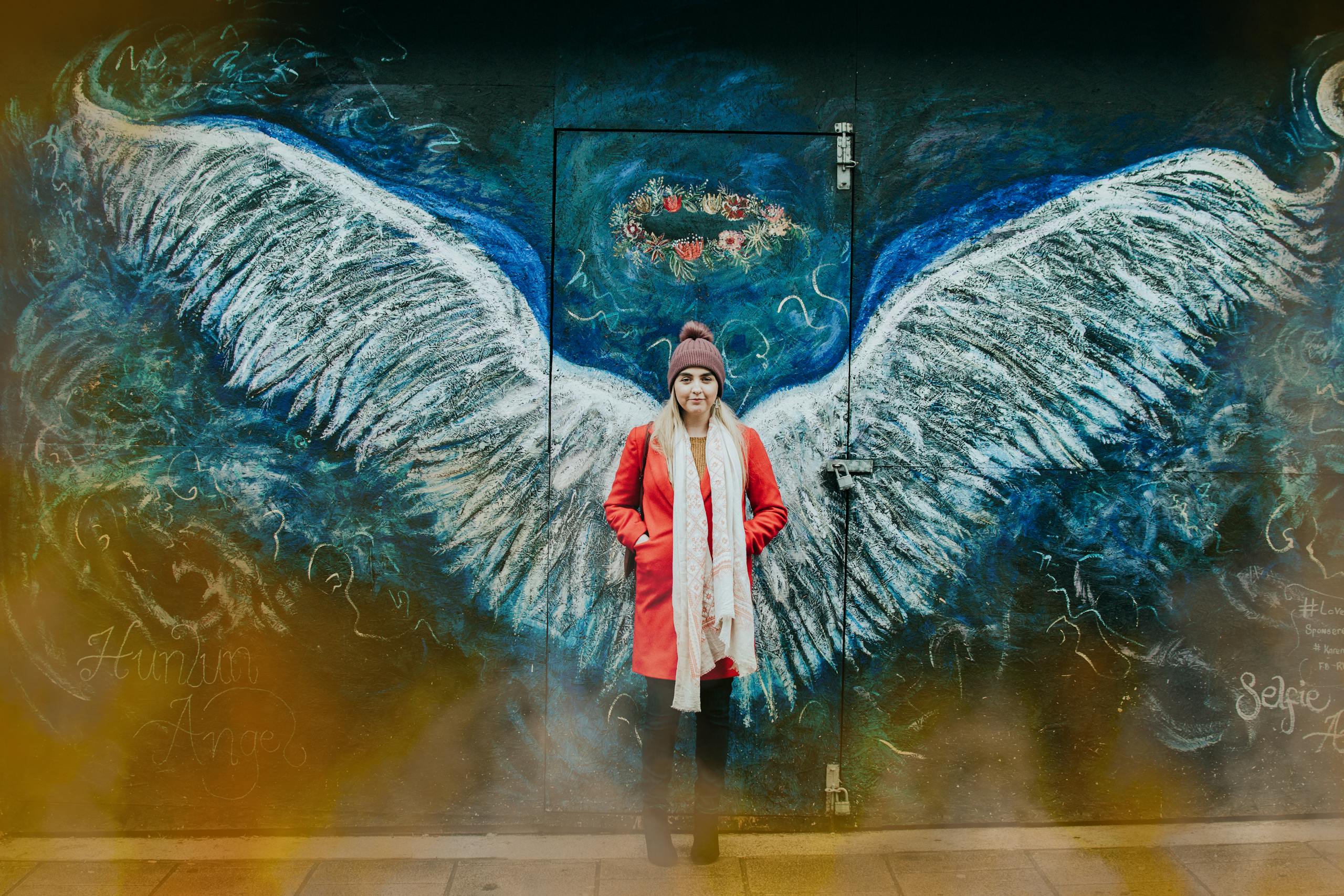 Photo by Lisa from Pexels Woman posing in front of angel wings street art in Bangor, Wales.